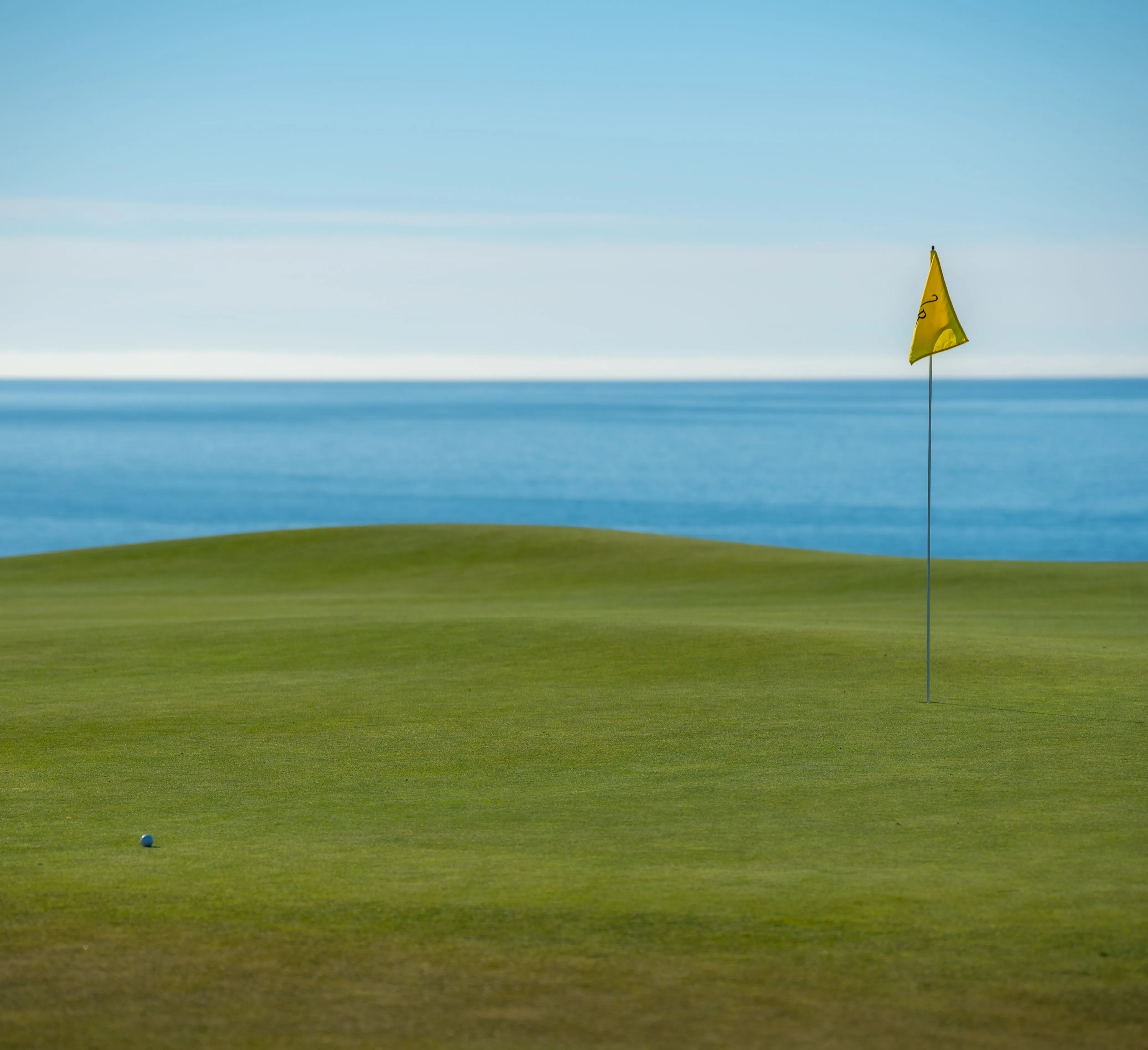 Green de golf junto al océano, con una bandera amarilla
